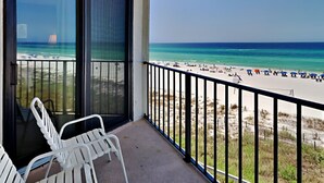 A balcony with white chairs, a view of a beach with people and umbrellas, and a clear blue sky. - Edgewater Tower II #303 | Balcony Views + Resort Amenities! (Panama City Beach)