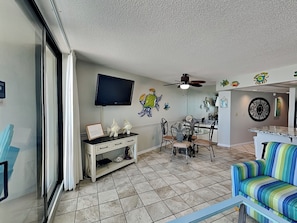 A living room with a TV, ceiling fan, dining table, chairs, and a colorful sofa.