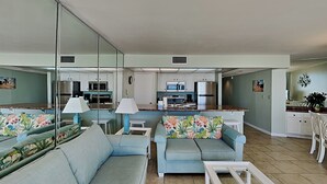 Una sala de estar con un sofá y sillones, una mesa de centro, y una cocina al fondo.