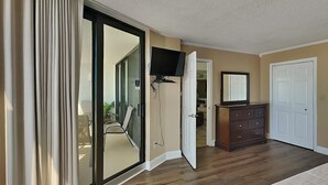 Un dormitorio con puerta de vidrio corrediza que da a un balcón, un aparador, una televisión y una puerta con espejo.