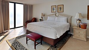 Een hotelkamer met een groot bed, een stoel, een nachtkastje en uitzicht op de oceaan.