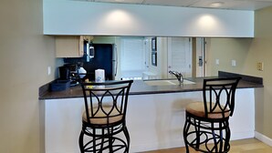 A modern kitchen with a central island, two bar stools, and a large window. - Edgewater Tower II #603 | Gulf-Front View + Amenities! (Panama City Beach)