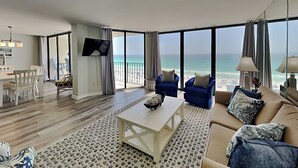 Un salon moderne doté d’un grand balcon, d’un téléviseur à écran plat, d’un coin repas et d’un canapé agrémenté de coussins décoratifs.