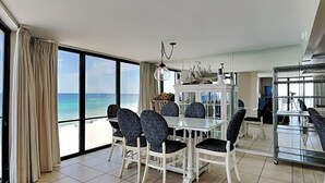 A dining area with a view of the ocean, a chandelier, and a white cabinet with decorative items.