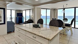 A modern kitchen with a granite countertop, white cabinetry, and a view of the ocean through large windows.