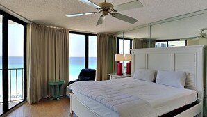 Ein Hotelzimmer mit einem großen Bett, einem Deckenventilator, einem Nachttisch mit Lampen, einem Sessel und Blick auf den Ozean.