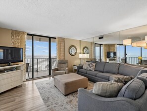 Un salon spacieux avec un grand canapé, un téléviseur et un balcon offrant une vue agréable.