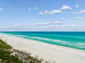 Une plage à l’eau turquoise et limpide, avec un rivage sablonneux et quelques parasols.
