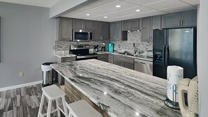 Una cocina moderna con armarios grises, encimera de mármol y electrodomésticos de acero inoxidable.