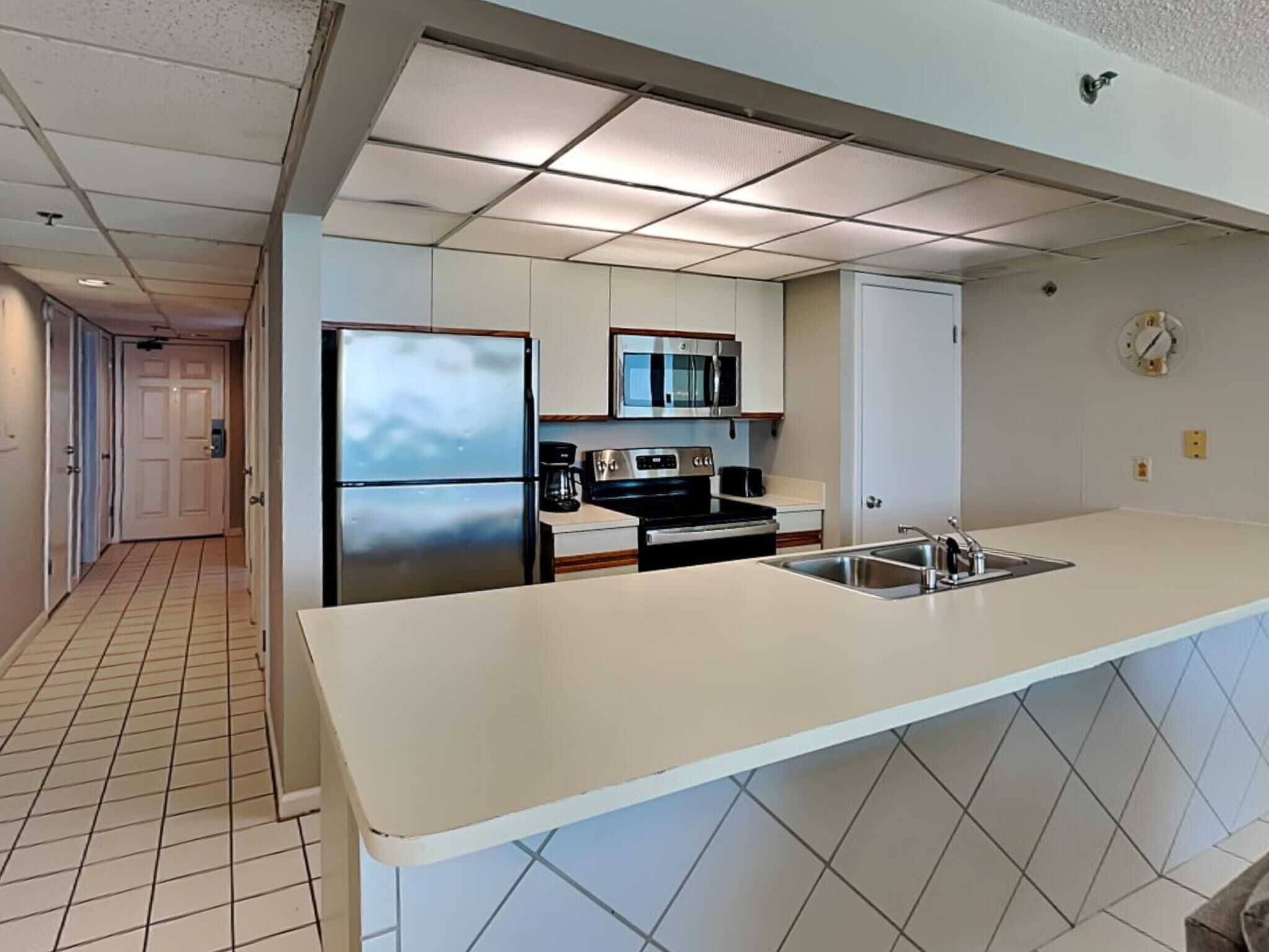 Cocina moderna con refrigerador de acero inoxidable, microondas y estufa, encimera blanca y salpicadero de azulejos.