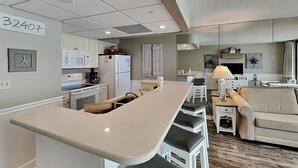 Una cocina moderna con armarios blancos, una isla central y un comedor con sofá y sillas.