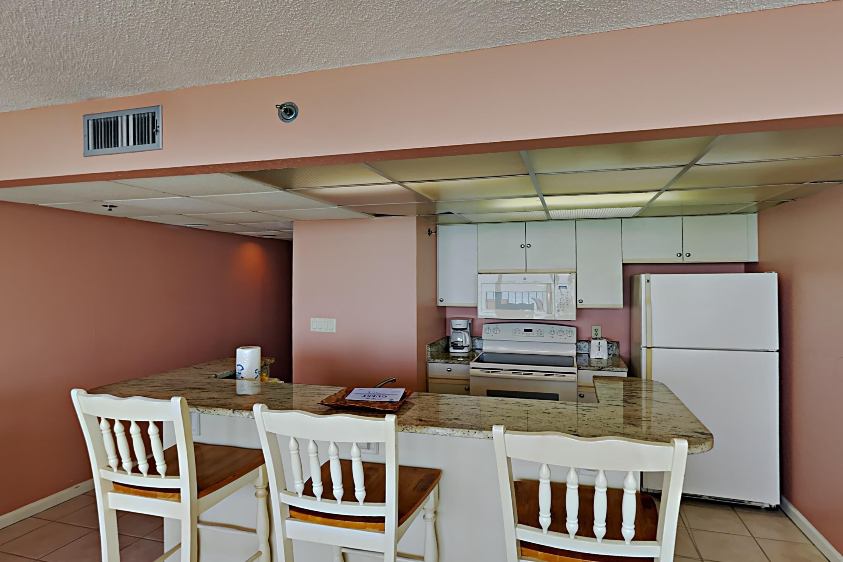 A kitchen with a granite countertop, white cabinetry, and a white refrigerator.