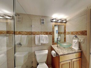 Un baño con ducha de vidrio, inodoro, lavabo de cristal y espejo sobre el lavabo.