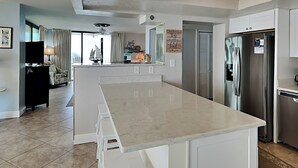 A modern kitchen with a large island, stainless steel appliances, and a view to the living area.