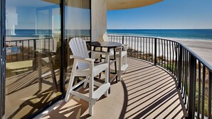 A balcony with a table and chairs, overlooking a beach.