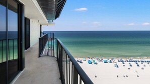 Un balcon avec vue sur l’océan et une plage parsemée de parasols.