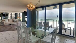 Ein geräumiger Wohnbereich mit einem Glastisch und weißen Stühlen, einem beigen Sofa und einer Chandelier.