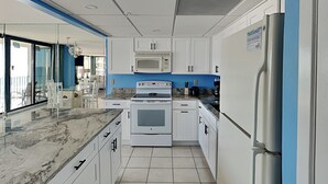 Eine moderne Küche mit weißen Schränken, einer Marmorarbeitsplatte, einem Backofen, einer Mikrowelle und einem Kühlschrank.