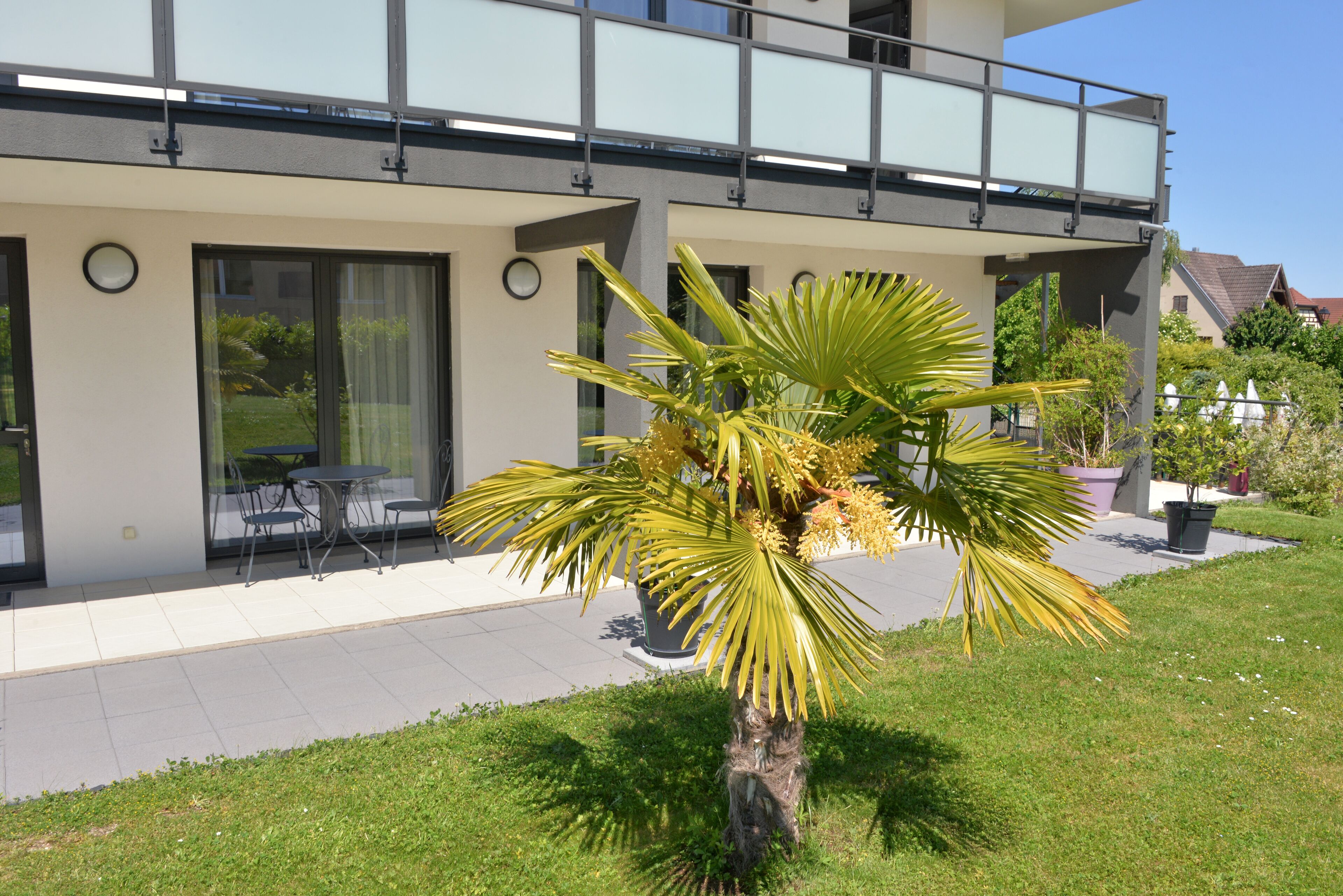 Una casa moderna de dos pisos con un balcón, un patio con mobiliario exterior y un césped bien cuidado.