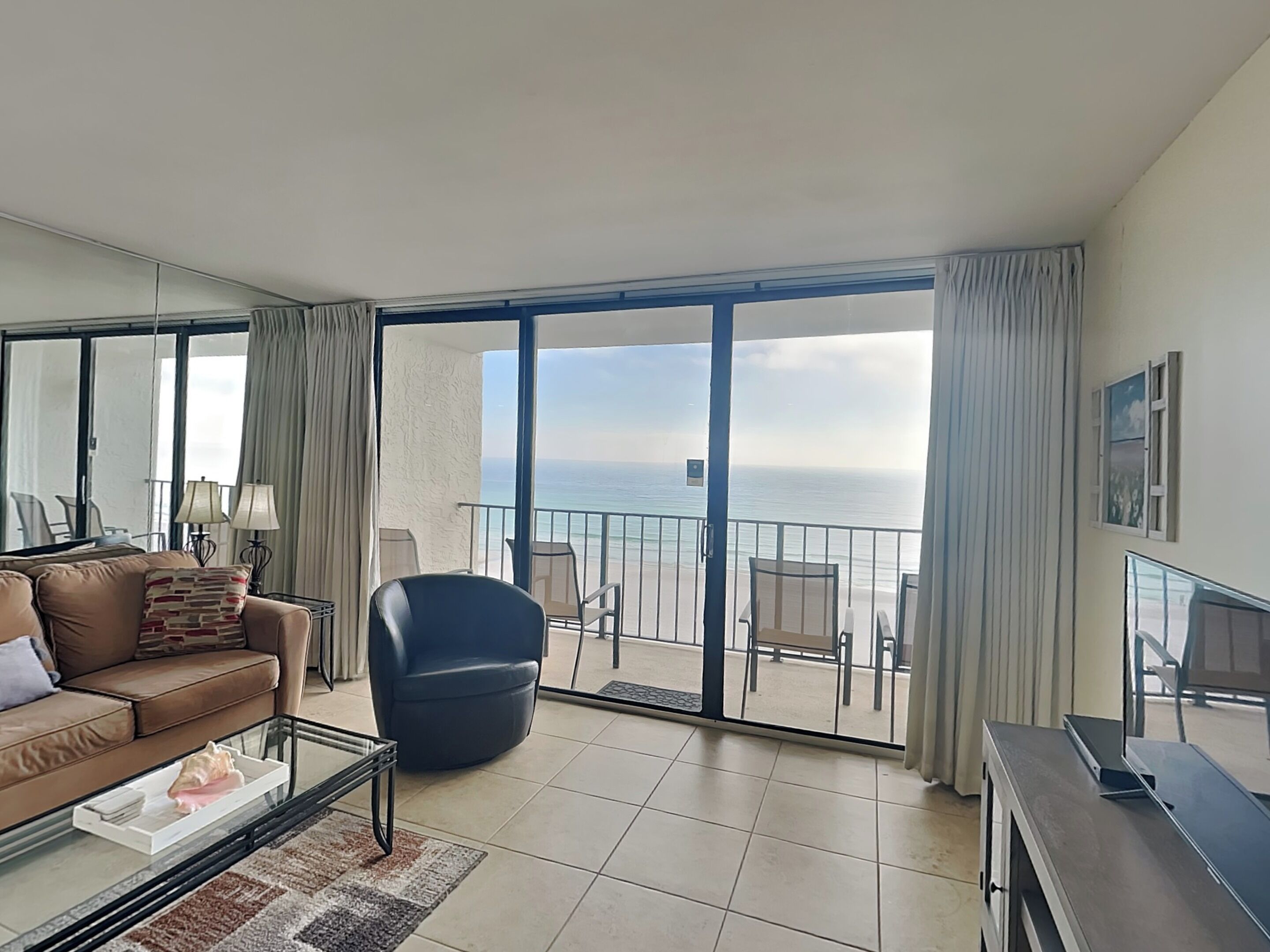 A spacious living room with a large sliding glass door leading to a balcony overlooking the sea.