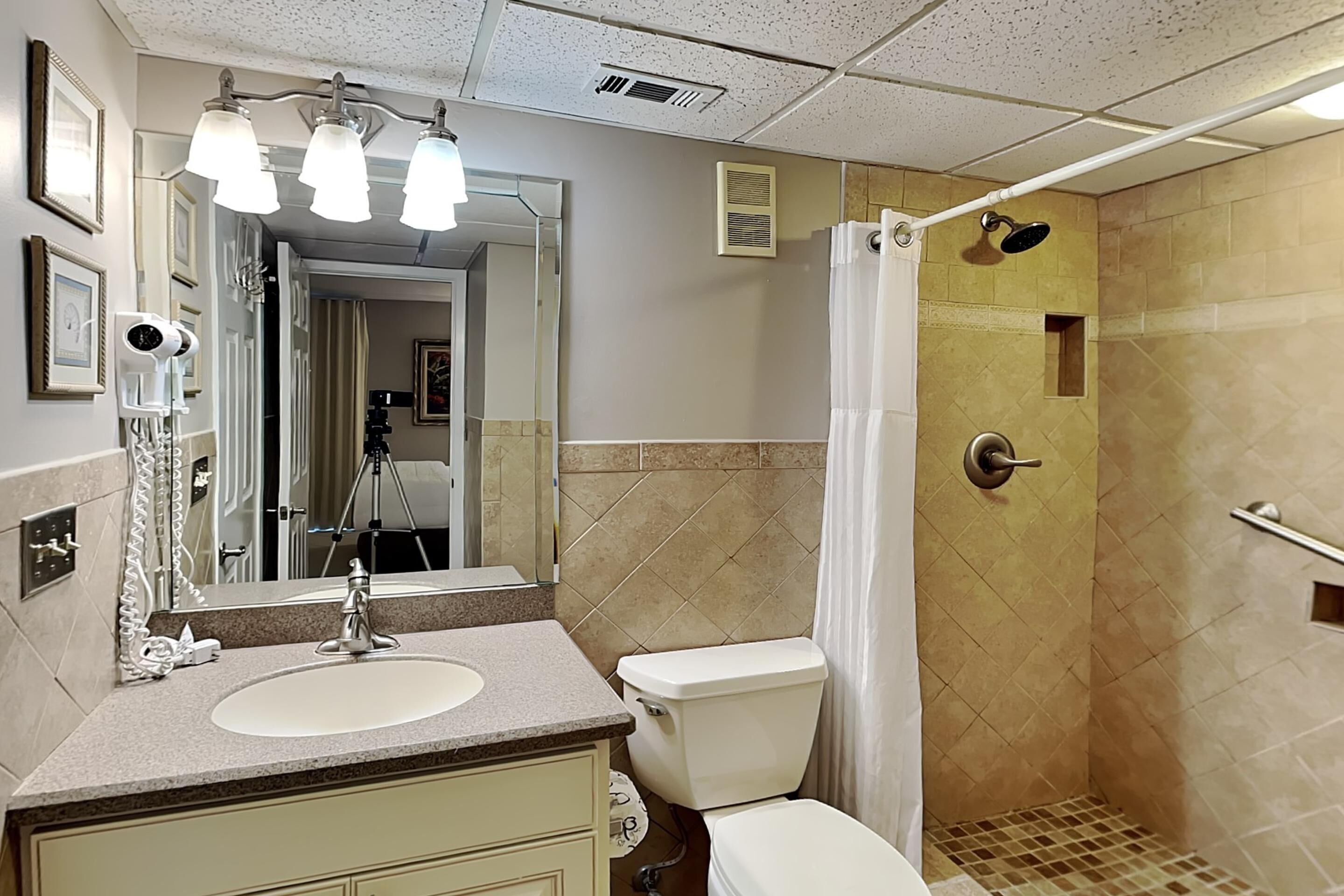 A bathroom with a sink, toilet, shower, and a mirror.
