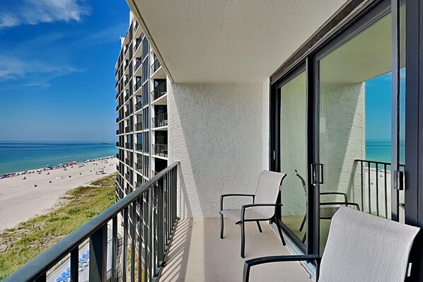 A balcony with two chairs, overlooking a beach and ocean.