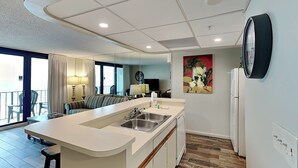 Uma cozinha moderna com uma ilha central, área de refeições com sofá e cadeiras, e uma janela grande com cortinas.