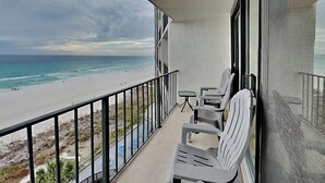 Varanda com vista para a praia e oceano. Há duas cadeiras e uma mesa pequena.