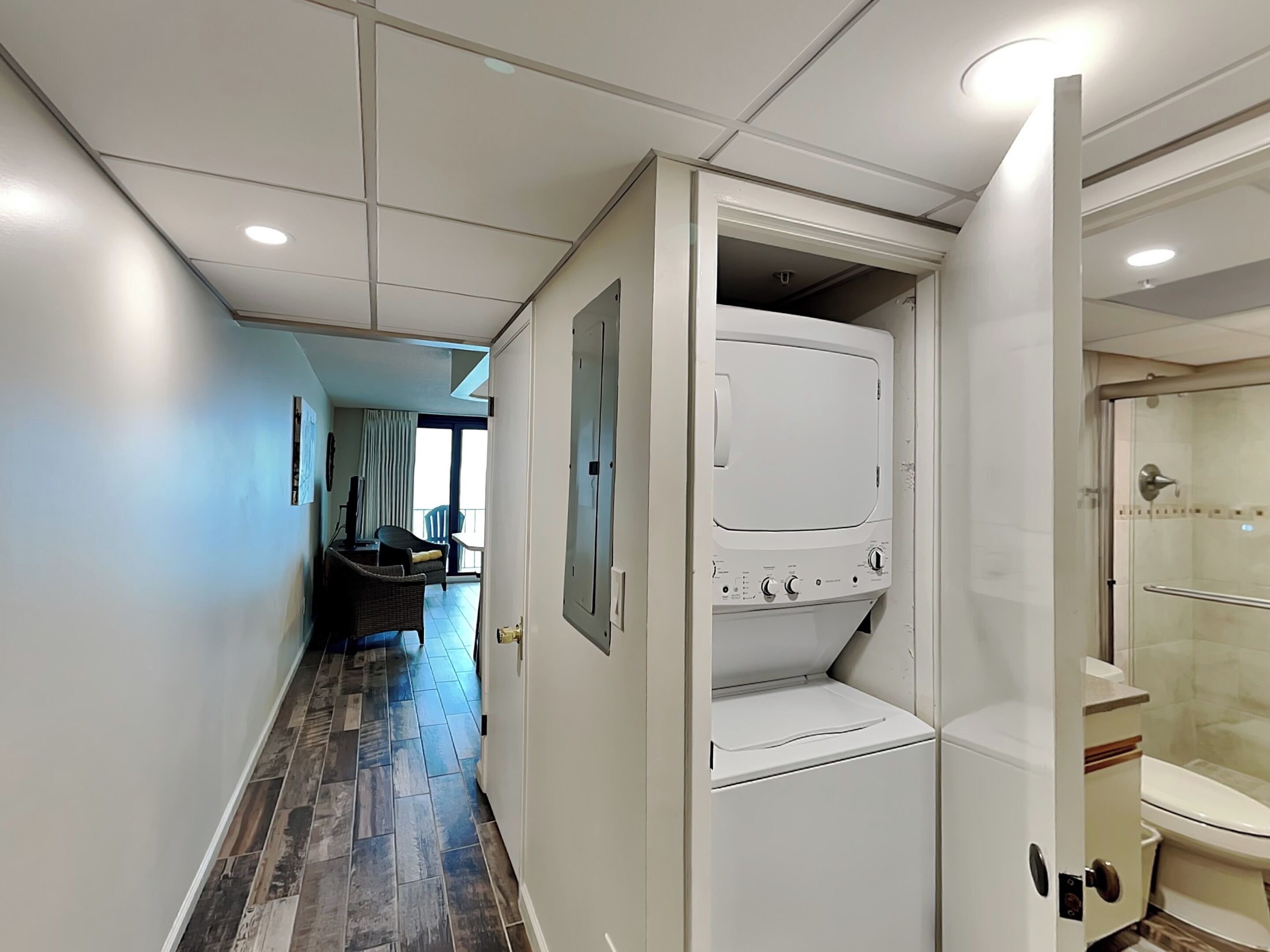 A hotel hallway with a laundry room, a shower area, and a balcony with a chair and table.