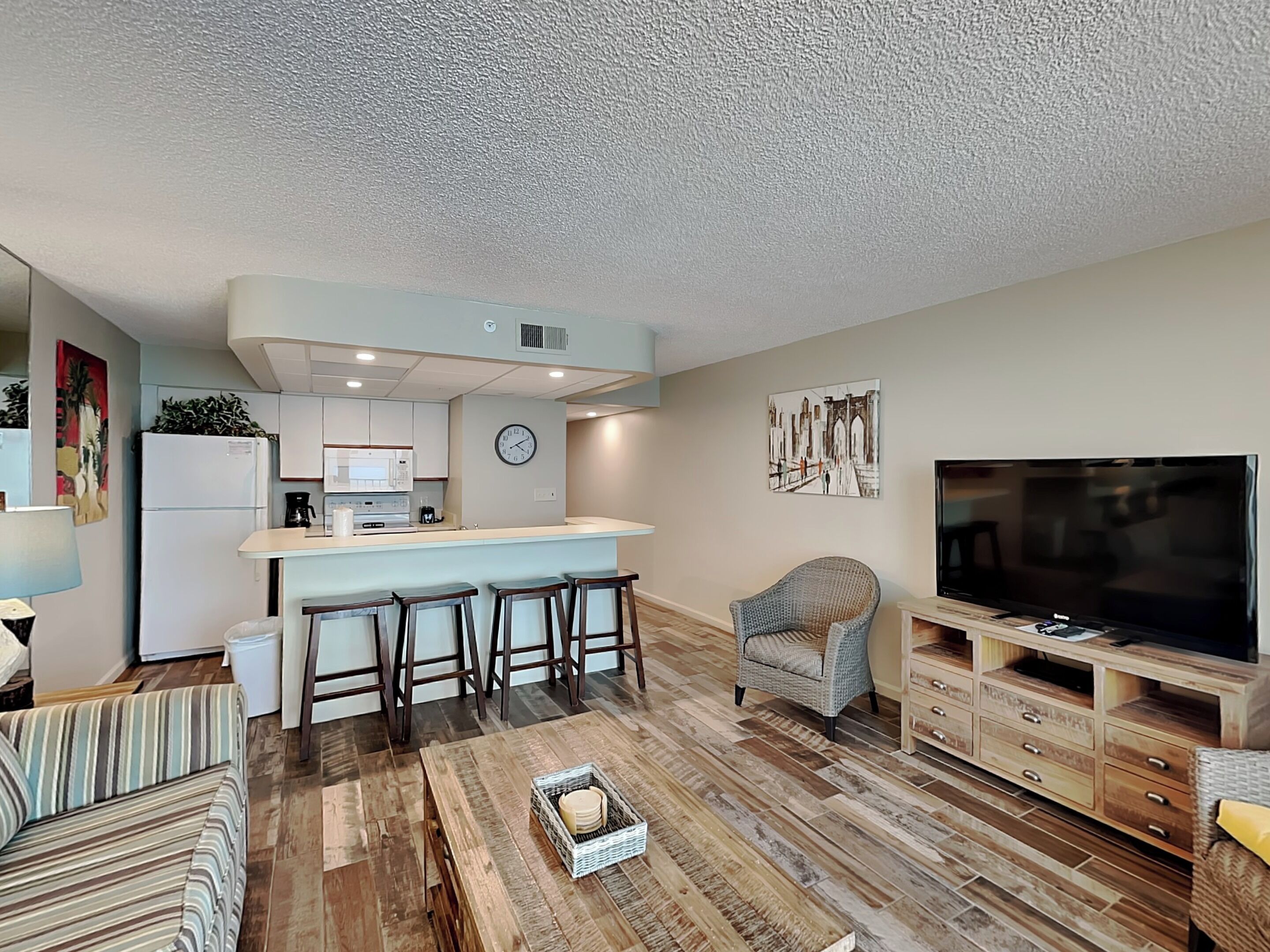 Un espacio habitable compacto con kitchenette, una zona de comedor con taburetes de bar, un área de estar con sofá y televisor.