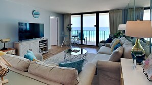 Ein modernes Wohnzimmer mit einem Flachbildfernseher, bequemen Sofas, einem Couchtisch und einem Balkon mit Meerblick.