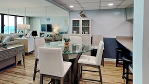 Ein modernes Wohnzimmer mit einem Glastisch, weißen Stühlen, einer Couch und einem Fernseher.