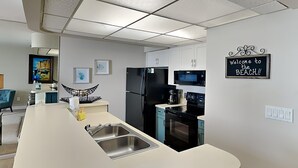 Een moderne keuken met een centraal eiland, een roestvrijstalen spoelbak, zwarte apparaten en een bord met de tekst 'Welcome to the Beach'.