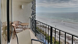 Een balkon met rieten stoelen en een tafel, met uitzicht op een strand met een hekwerk en een zeegezicht.