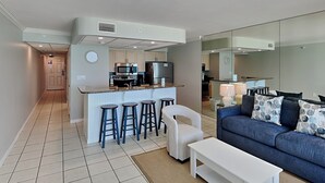 A modern apartment with a kitchen, a living area with a sofa and a coffee table, and a small bar area with stools.