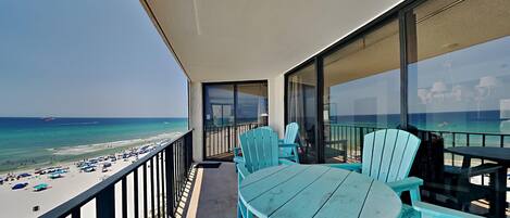 Un balcon avec vue sur la plage, des chaises turquoise et une table.