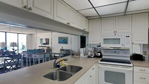 A modern kitchen with white cabinets, a double sink, a microwave, and a stove. - Edgewater Tower III #804 | Beachside Pool + Views! (Panama City Beach)