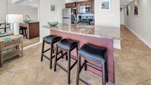 Una cocina moderna con una isla central, taburetes de bar y un comedor con lámpara y mesa.
