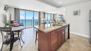 Una cocina amplia con una isla grande, un comedor con mesa y sillas, y un balcón con vista al océano.