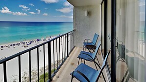 A balcony with a view of a beach and ocean, featuring a railing, a chair, and a table. - Edgewater Tower III #910 | Gulf Front + Amenities (Panama City Beach)