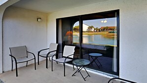Varanda com quatro cadeiras e uma mesa pequena, com vista para um corpo de água e paisagem distante.