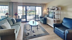 Un salon moderne comprenant un canapé, un fauteuil, un meuble pour la télévision et un balcon offrant une vue sur la ville.