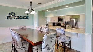 A dining area with a wooden table and patterned chairs, a kitchen with white cabinets and stainless steel appliances, and a ceiling light fixture.
