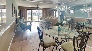 Ein geräumiges Wohnzimmer mit einem großen Glastisch, umgeben von Stühlen, einer Couch und einem Balkon mit Aussicht.