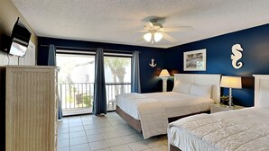Une chambre d’hôtel avec deux lits, un ventilateur de plafond, une télévision et un balcon avec des rideaux.