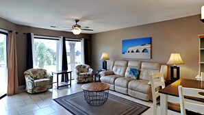 Un salon avec un canapé beige, deux fauteuils, une table basse et une table à manger avec des chaises.
