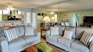 A living room with two grey sofas, a coffee table, and a large mirror reflecting the room. - Edgewater Villa #1501 | Golf Course View! (Panama City Beach)