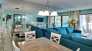 Una sala de estar moderna con sofás color turquesa, una mesa de comedor de madera y un espejo grande.