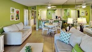 A living room with a sofa, a coffee table, and a dining area with a table and chairs. - Edgewater Villa #1702 | Golf View and Resort Amenities (Panama City Beach)