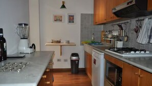 Une cuisine avec des meubles de rangement en bois, une cuisinière à gaz, un lave-vaisselle et un mixeur posés sur le plan de travail.